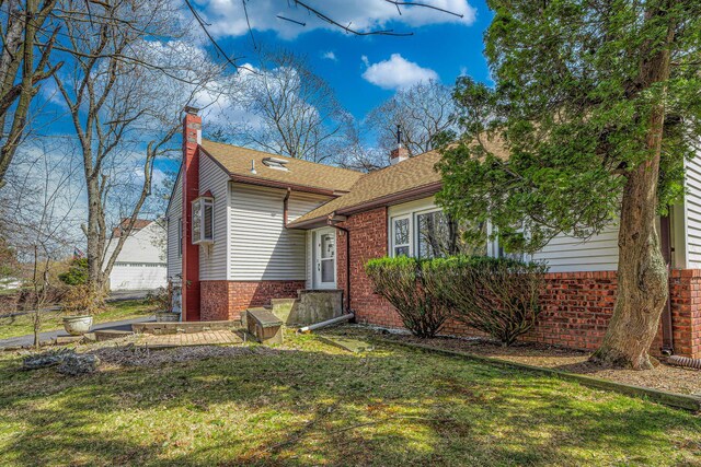 view of front of house with roof with shingles, a chimney, a front yard, and brick siding