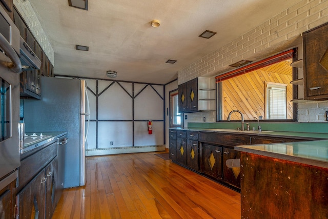 kitchen with dark brown cabinetry, brick wall, hardwood / wood-style floors, a baseboard radiator, and stovetop
