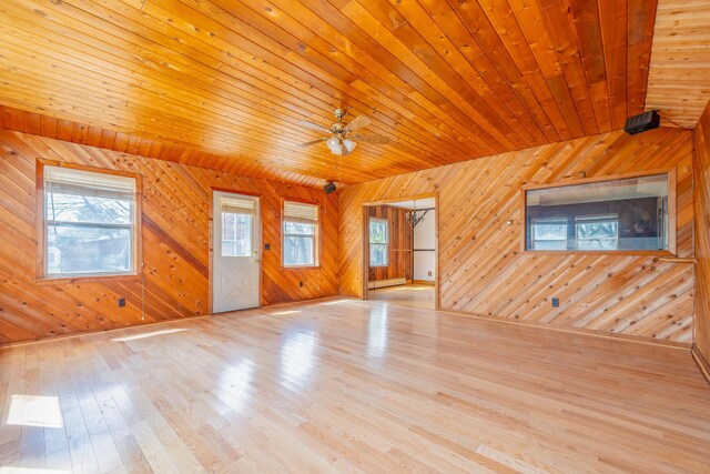 unfurnished living room with a baseboard heating unit, a ceiling fan, wood walls, wood ceiling, and wood finished floors