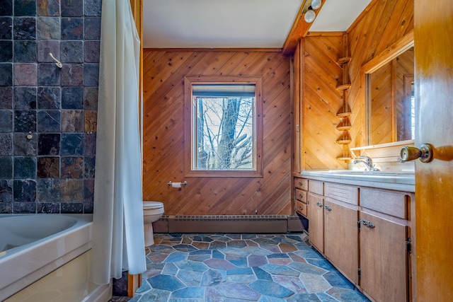 full bathroom featuring vanity, wooden walls, toilet, stone finish flooring, and a baseboard radiator