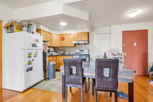 kitchen with light wood finished floors, under cabinet range hood, stainless steel range with gas stovetop, freestanding refrigerator, and decorative backsplash