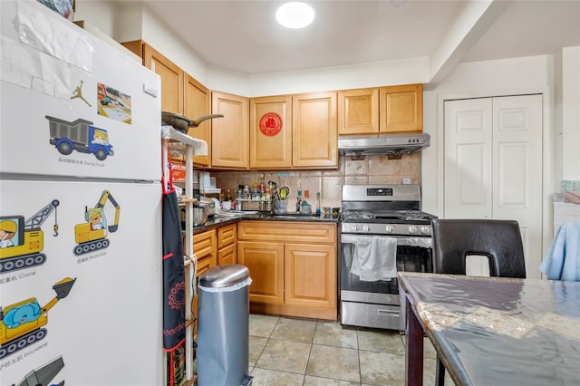 kitchen featuring under cabinet range hood, stainless steel gas stove, light tile patterned flooring, freestanding refrigerator, and tasteful backsplash