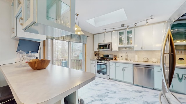 kitchen featuring white cabinets, appliances with stainless steel finishes, a sink, backsplash, and a skylight