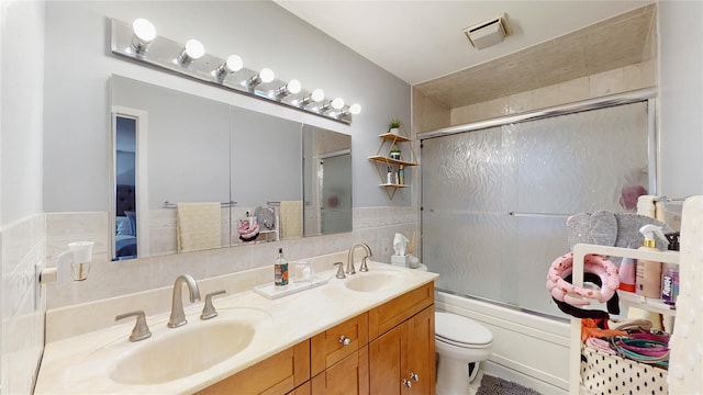 bathroom featuring visible vents, double vanity, toilet, a sink, and combined bath / shower with glass door
