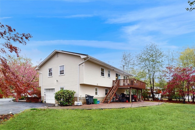 back of property with driveway, a wooden deck, a yard, an attached garage, and stairs