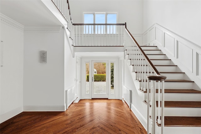 foyer entrance with crown molding, a towering ceiling, stairway, wood finished floors, and baseboards