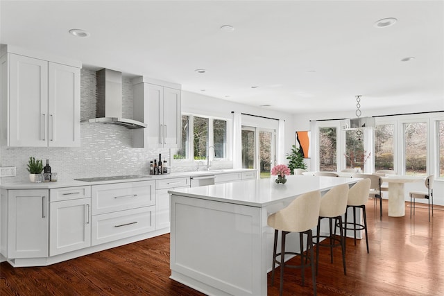 kitchen featuring tasteful backsplash, wall chimney range hood, light countertops, a kitchen island, and black electric cooktop