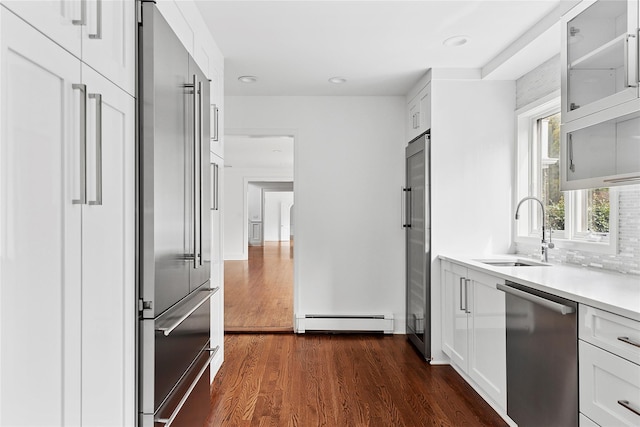 kitchen with baseboard heating, light countertops, dark wood-type flooring, stainless steel appliances, and a sink