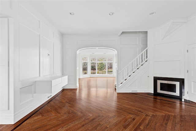 unfurnished living room featuring a decorative wall, ornamental molding, recessed lighting, stairway, and a fireplace with flush hearth