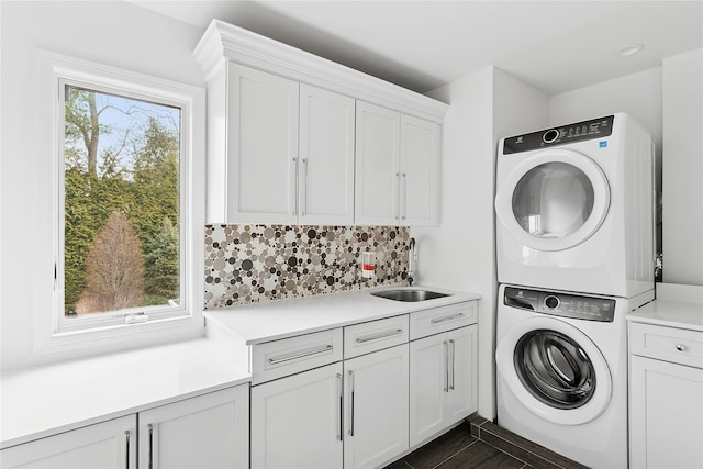 laundry area featuring stacked washer and dryer, a sink, cabinet space, and a healthy amount of sunlight