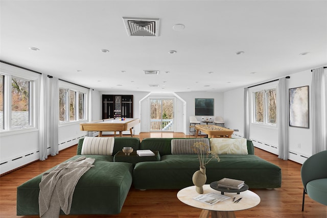 living room featuring plenty of natural light, visible vents, baseboard heating, and wood finished floors