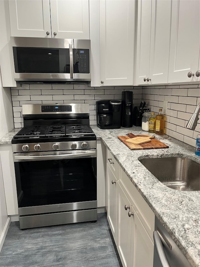 kitchen with backsplash, white cabinets, light stone countertops, stainless steel appliances, and a sink