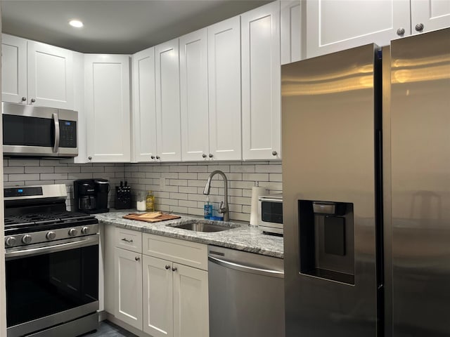 kitchen with tasteful backsplash, a sink, white cabinetry, light stone countertops, and stainless steel appliances