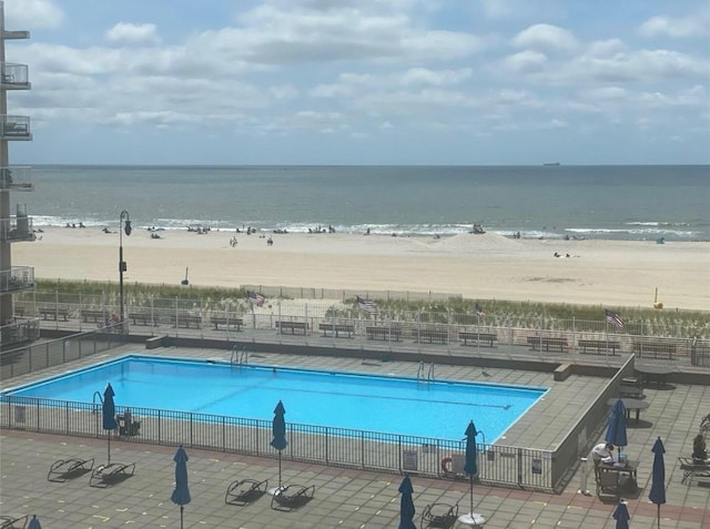 view of swimming pool featuring a water view, fence, and a beach view