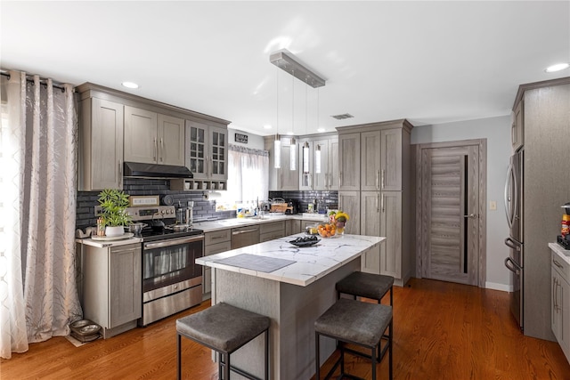 kitchen featuring appliances with stainless steel finishes, gray cabinetry, light countertops, a breakfast bar, and under cabinet range hood