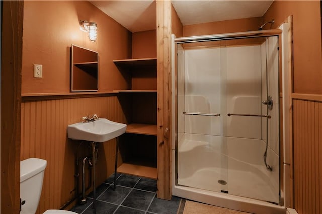bathroom with tile patterned floors, toilet, a shower stall, wainscoting, and a sink