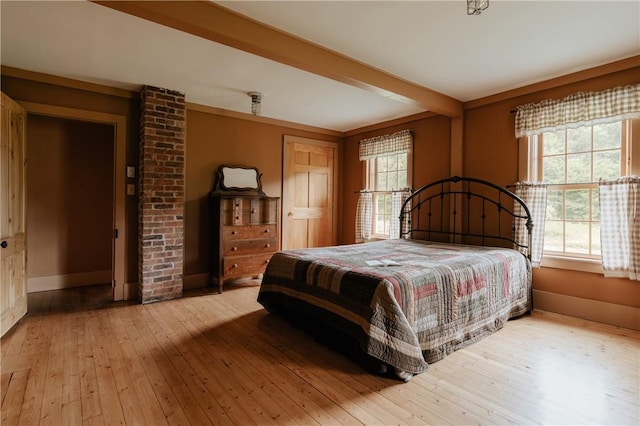 bedroom with beam ceiling, baseboards, multiple windows, and wood-type flooring