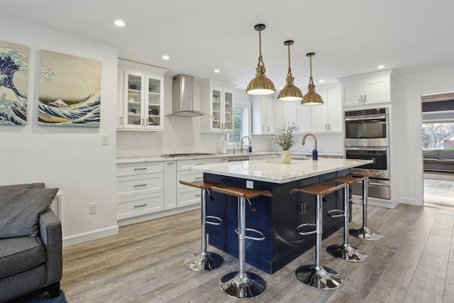kitchen featuring white cabinets, wall chimney exhaust hood, appliances with stainless steel finishes, and an island with sink