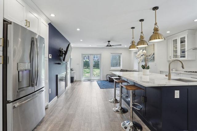 kitchen featuring light stone counters, a sink, light wood-type flooring, stainless steel refrigerator with ice dispenser, and recessed lighting