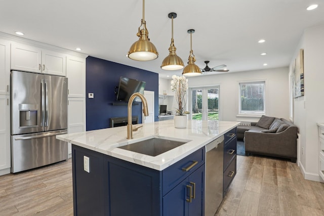 kitchen with stainless steel appliances, a sink, light wood-type flooring, open floor plan, and white cabinetry
