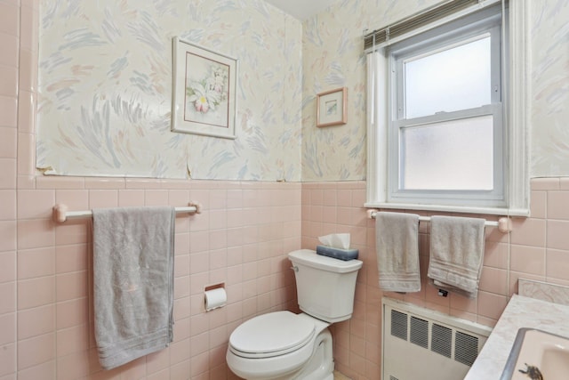bathroom with a wainscoted wall, toilet, tile walls, radiator heating unit, and wallpapered walls