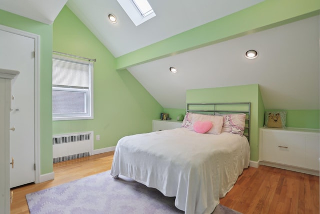 bedroom featuring radiator heating unit, vaulted ceiling with skylight, wood finished floors, baseboards, and recessed lighting