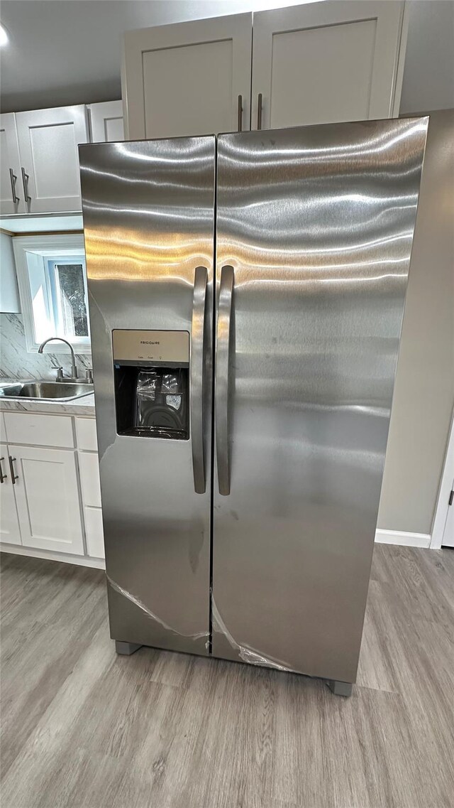 734 Cooley Rd, Parksville, NY 12768 - detailed view of stainless steel refrigerator with ice dispenser, light wood-style flooring, white cabinetry, backsplash, and light countertops