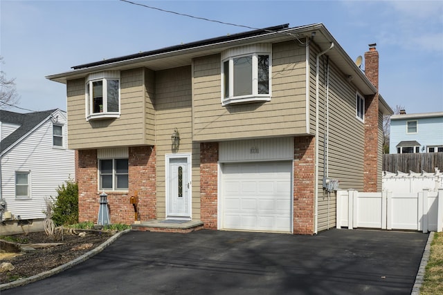 view of front of home with aphalt driveway, fence, brick siding, an attached garage, and a chimney