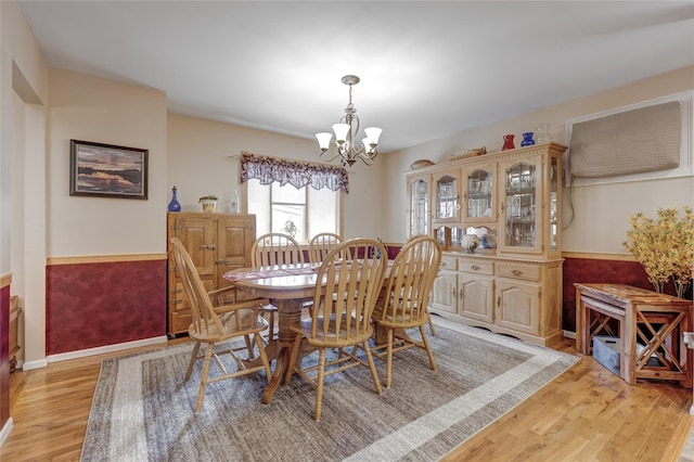 dining space featuring light wood-style flooring, a notable chandelier, and wainscoting