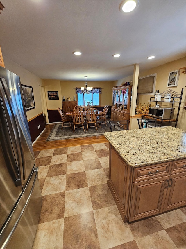kitchen featuring recessed lighting, freestanding refrigerator, an inviting chandelier, and light stone counters