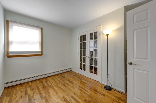 spare room featuring light wood finished floors, french doors, and a baseboard heating unit