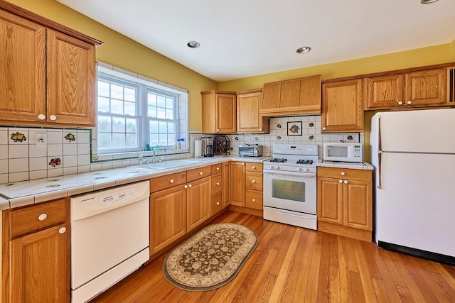 kitchen featuring white appliances, tile counters, light wood-type flooring, tasteful backsplash, and a sink