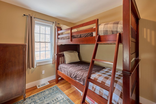 bedroom with visible vents, baseboards, wood finished floors, and multiple windows
