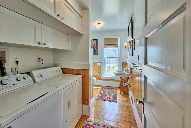 laundry area featuring light wood-style floors, separate washer and dryer, wainscoting, and cabinet space