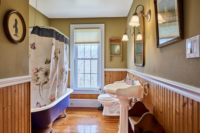 full bath with wainscoting, toilet, wood walls, wood finished floors, and a soaking tub