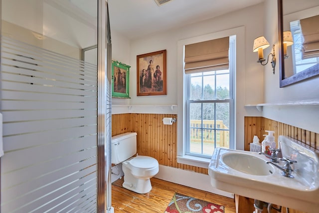 bathroom with wood finished floors, toilet, wooden walls, a wainscoted wall, and a sink