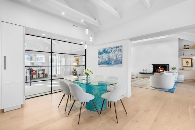 dining room with recessed lighting, a towering ceiling, a warm lit fireplace, and hardwood / wood-style floors