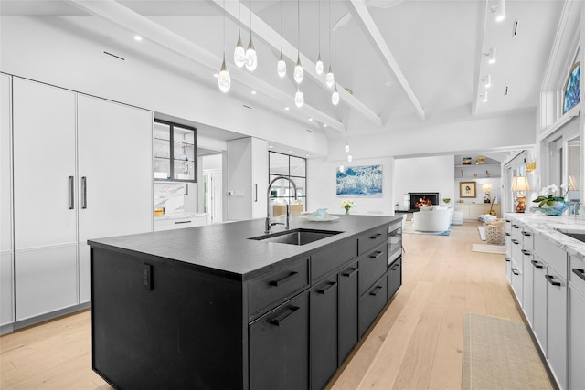 kitchen with white cabinets, a sink, a kitchen island with sink, dark cabinets, and open floor plan