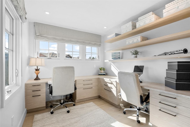 home office with baseboards, light wood finished floors, and built in desk