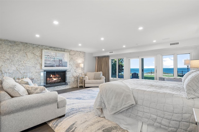 bedroom with visible vents, access to exterior, a stone fireplace, recessed lighting, and a water view