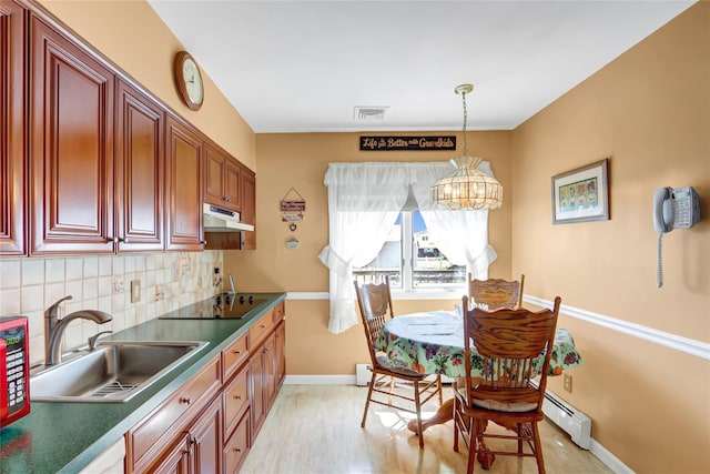 kitchen featuring baseboard heating, black electric cooktop, under cabinet range hood, decorative backsplash, and a sink