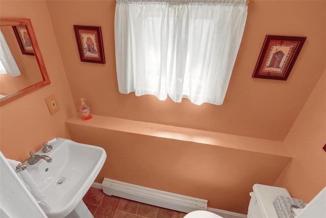 half bath with toilet, a baseboard heating unit, and a sink