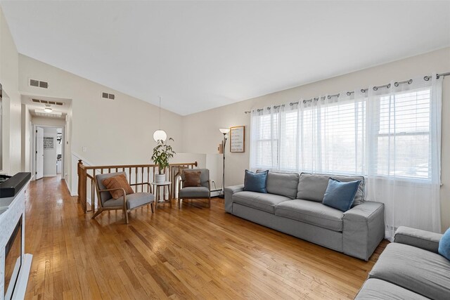 living area featuring lofted ceiling, visible vents, light wood finished floors, and a wealth of natural light