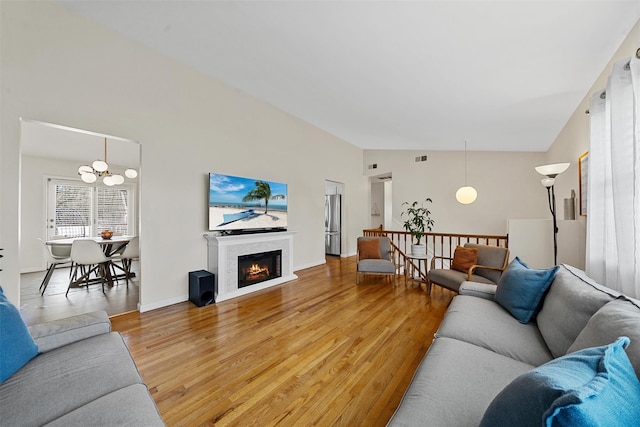 living room featuring light wood-type flooring, vaulted ceiling, a glass covered fireplace, and a chandelier