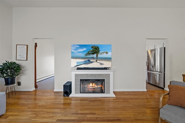 living room featuring baseboards, a glass covered fireplace, wood finished floors, and baseboard heating