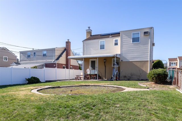 rear view of house featuring stucco siding, a chimney, solar panels, a fenced backyard, and a lawn