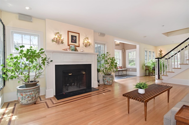 living area with stairs, recessed lighting, a fireplace with flush hearth, and light wood-style floors