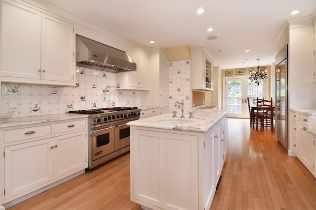 kitchen featuring ventilation hood, white cabinets, a sink, light wood-style flooring, and premium appliances