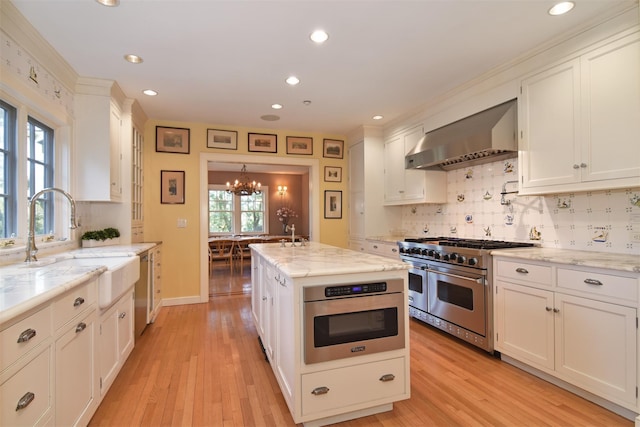 kitchen with wall chimney exhaust hood, a chandelier, white cabinets, a sink, and appliances with stainless steel finishes