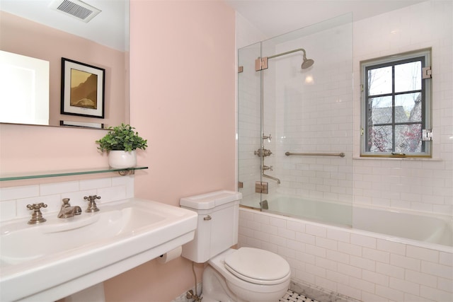 bathroom with tiled shower / bath combo, toilet, visible vents, and a sink